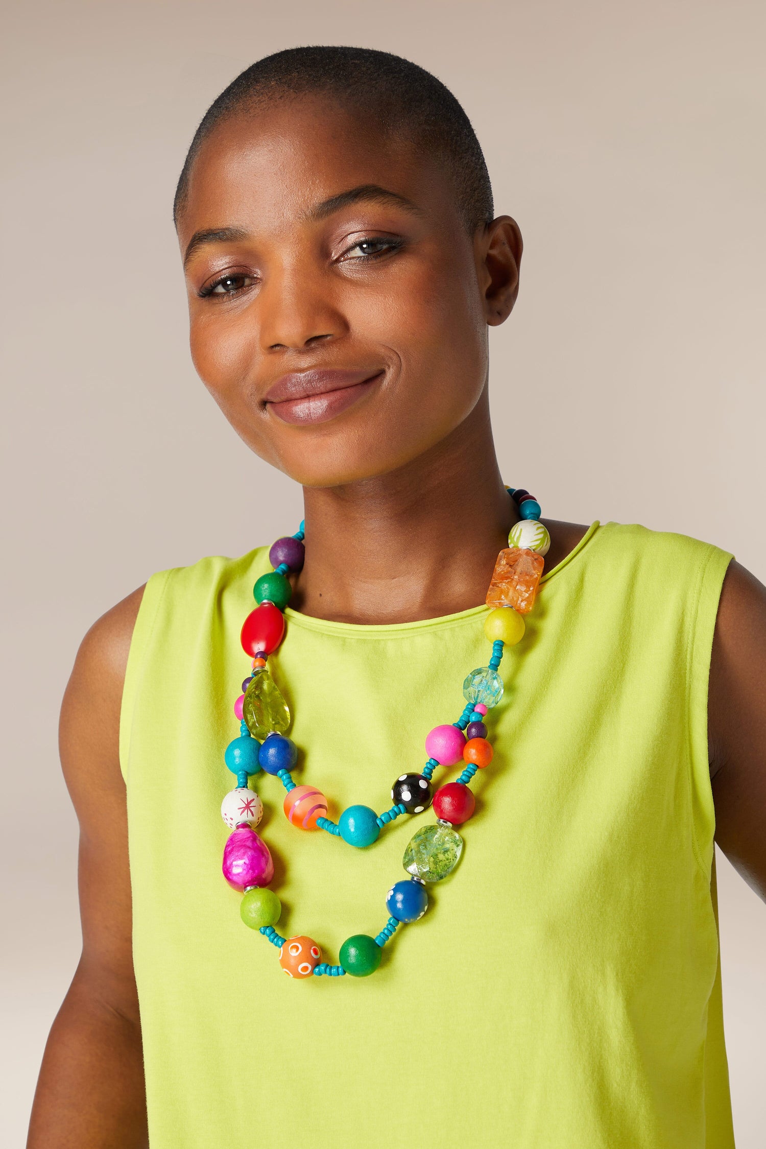 A confident black woman in a lime green top smiles gently, wearing a vibrant Colour Pop Rainbow Spheres Necklace.