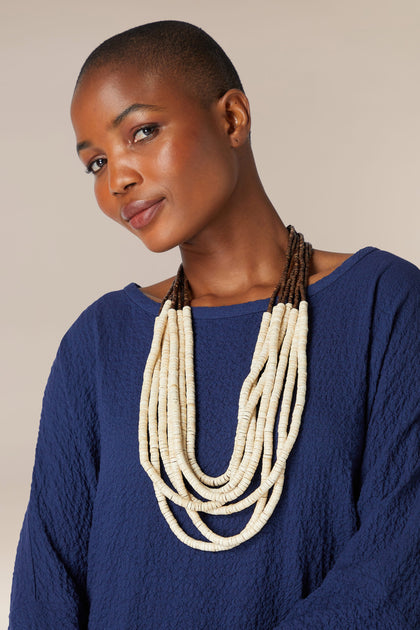 A woman with a short haircut wearing a blue sweater and a Freshwater Pearl Necklace, posing against a neutral background.