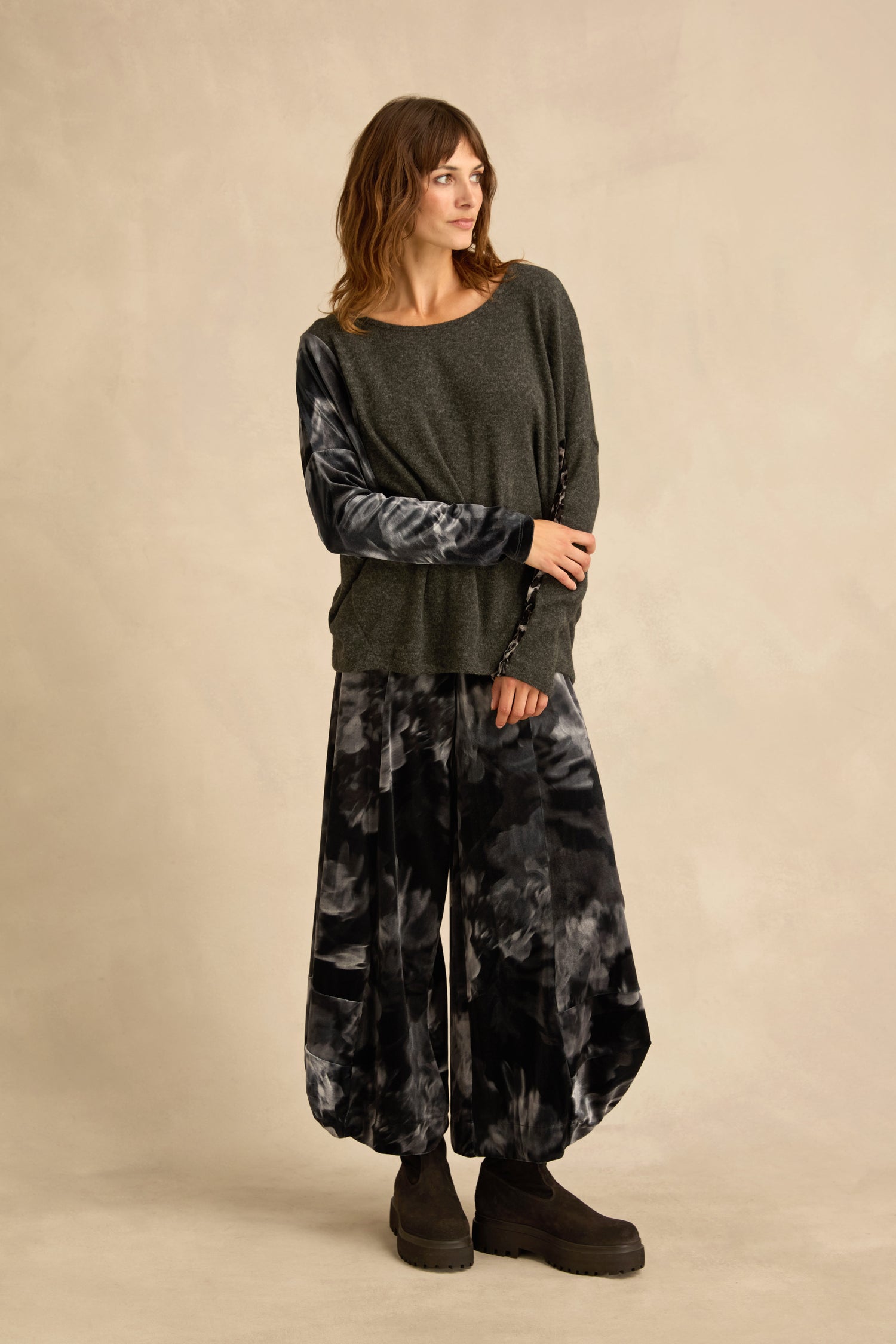 A woman stands against a beige backdrop wearing the Blurred Floral Jersey Top, paired with wide-leg tie-dye pants and black platform shoes.