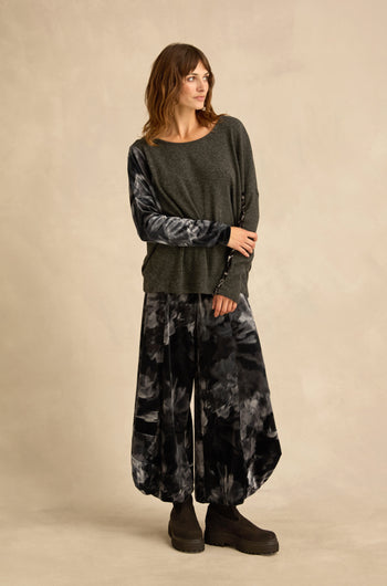 A woman stands against a beige backdrop wearing the Blurred Floral Jersey Top, paired with wide-leg tie-dye pants and black platform shoes.
