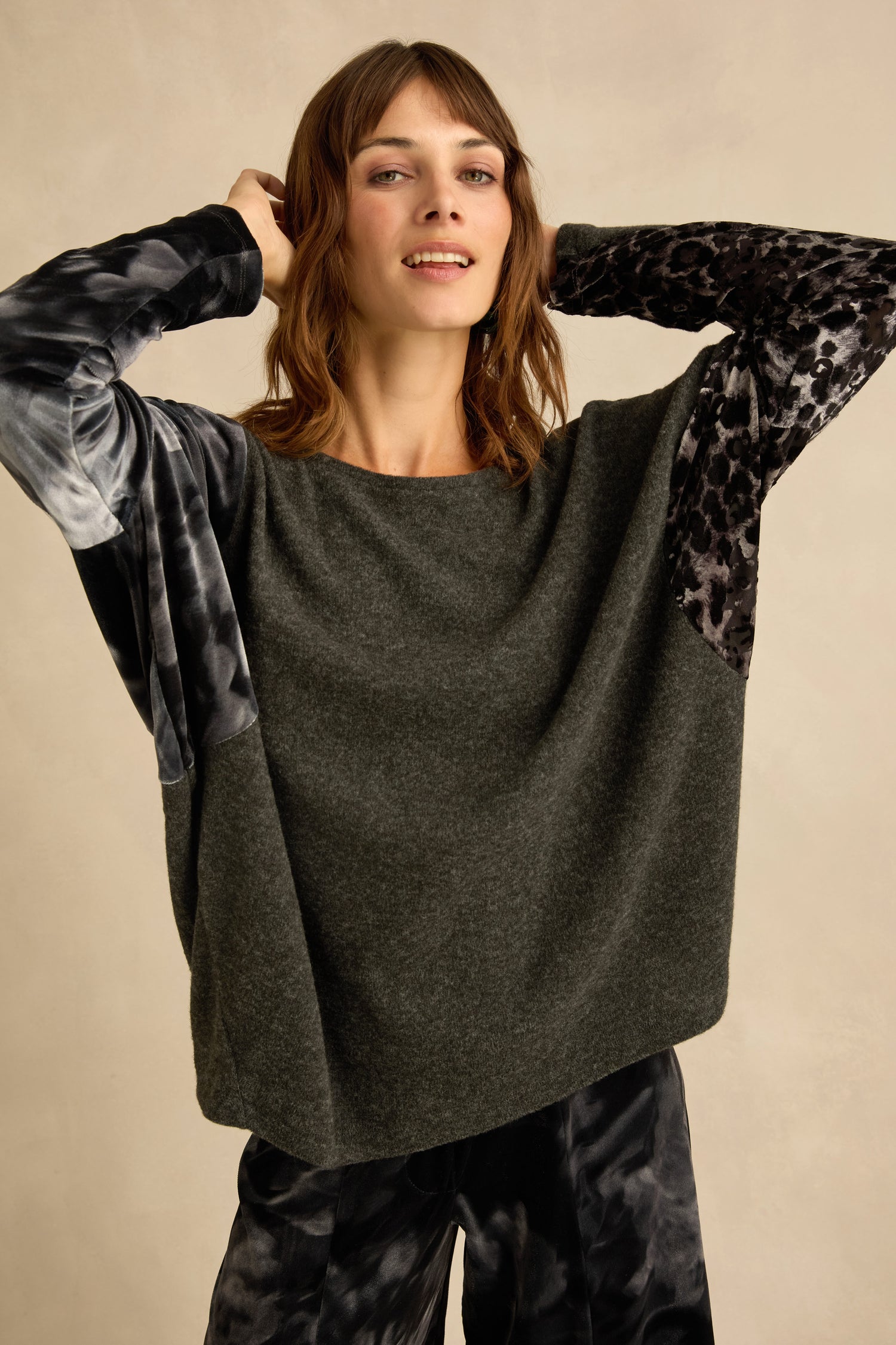 A woman wearing the Blurred Floral Jersey Top—a loose, charcoal grey sweater featuring printed sleeves—and matching patterned pants, standing against a neutral background.