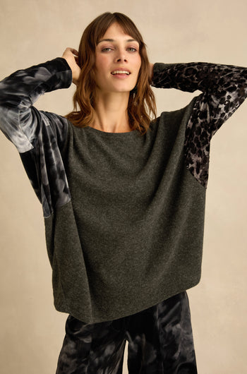 A woman wearing the Blurred Floral Jersey Top—a loose, charcoal grey sweater featuring printed sleeves—and matching patterned pants, standing against a neutral background.