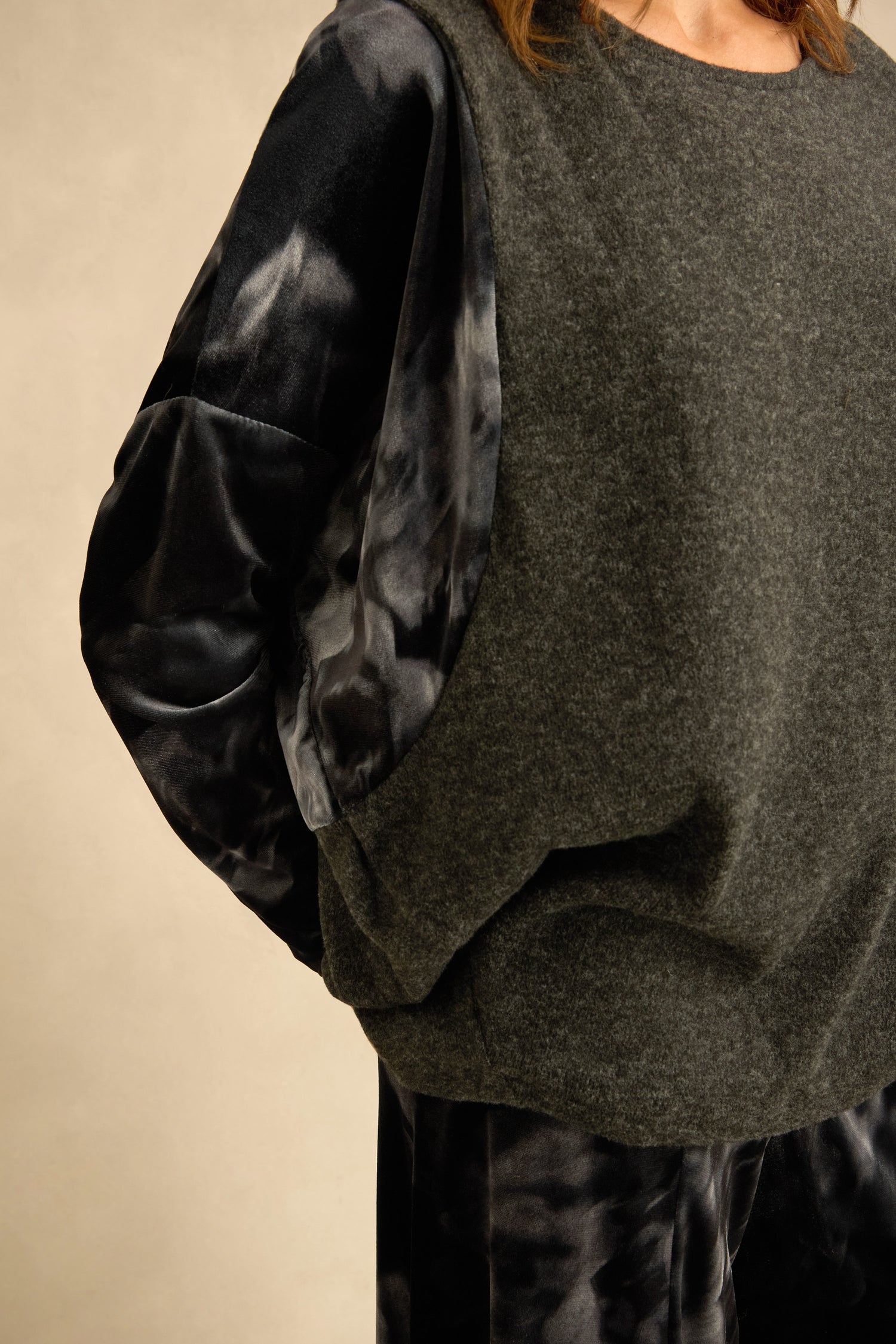 A person wearing the Blurred Floral Jersey Top—a black and gray tie-dye long-sleeve shirt with printed sleeves—layered under a charcoal grey sleeveless sweater and paired with matching pants, stands against a neutral background.