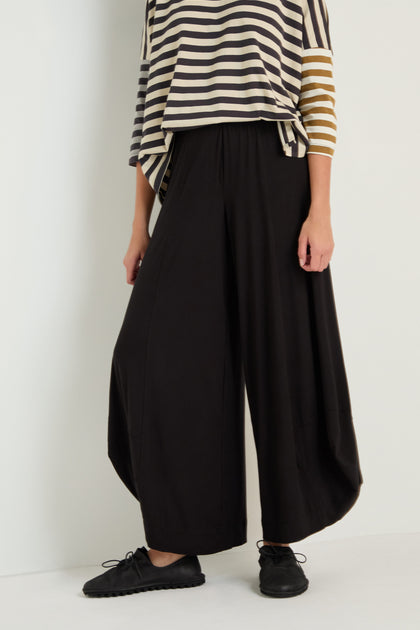 Person wearing a black and beige striped top with asymmetrical sleeves, Bubble Hem Trousers in black, and black shoes, standing against a plain backdrop.