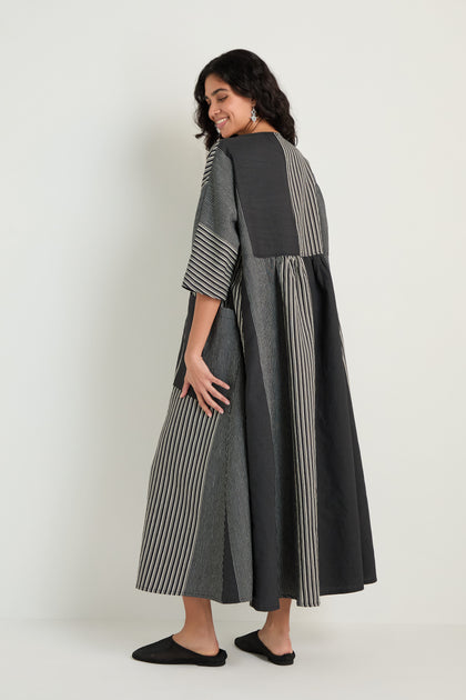 A woman stands sideways, wearing the Mixed Stripe Easy Dress with vertical stripes and three-quarter sleeves, paired with black slip-on shoes.