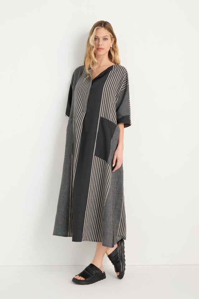 A woman stands sideways, wearing the Mixed Stripe Easy Dress with vertical stripes and three-quarter sleeves, paired with black slip-on shoes.