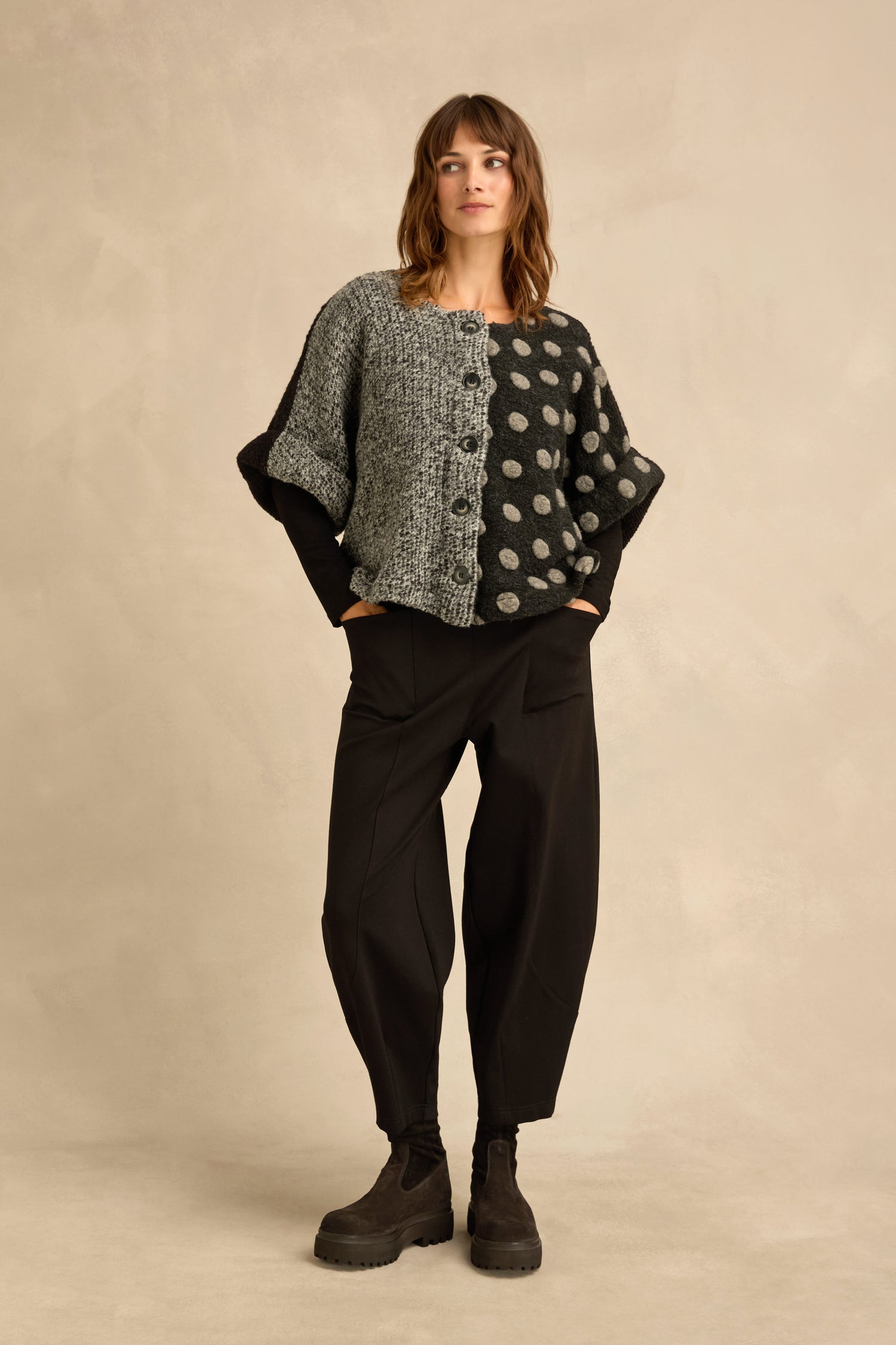 Woman stands against a beige backdrop wearing the Sleeveless Spot Jacket, paired with black loose pants and chunky boots.