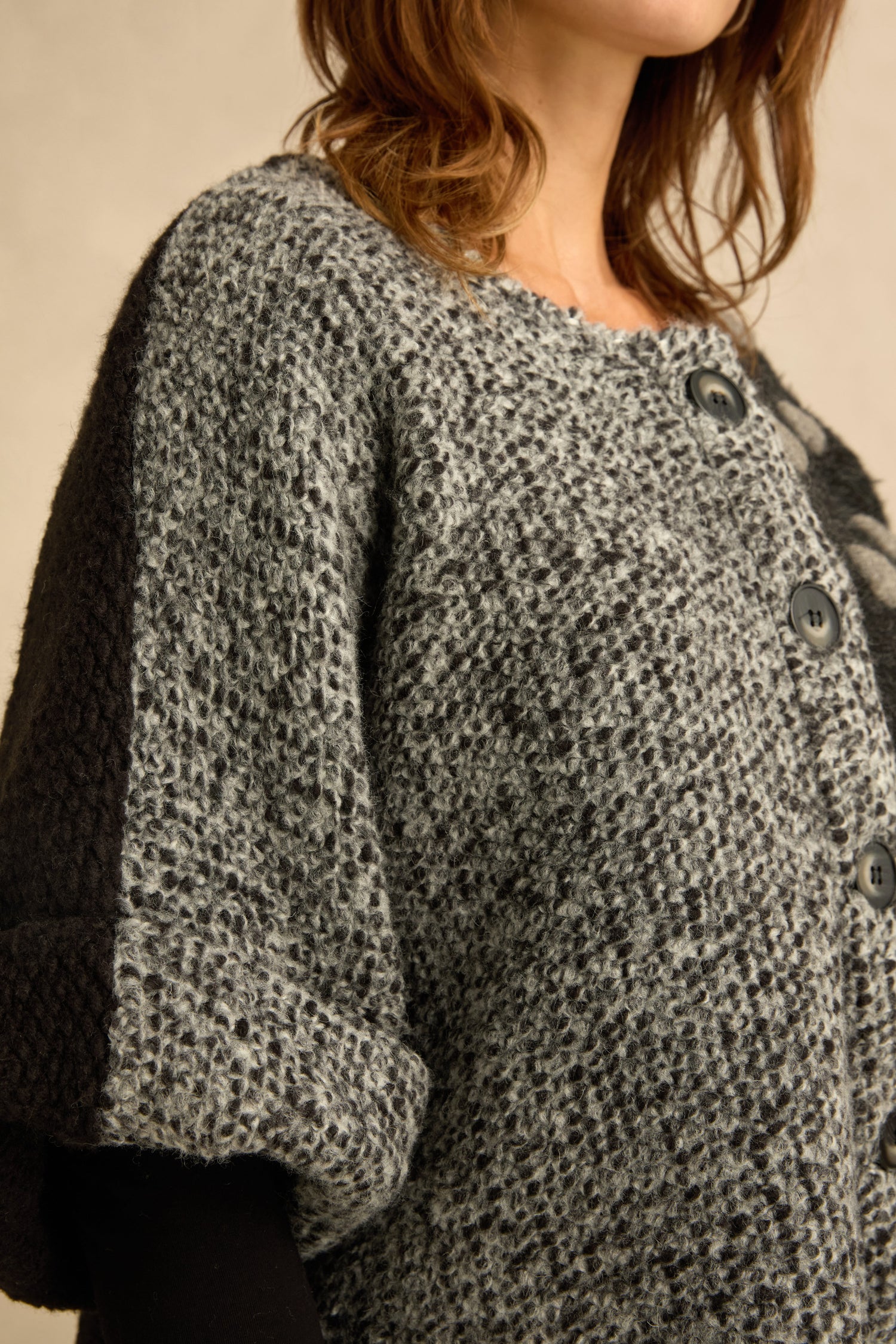 A person wearing the Sleeveless Spot Jacket, a gray and black mixed textured knit coat with buttons, shown from shoulders to mid-torso and facing slightly to the side.