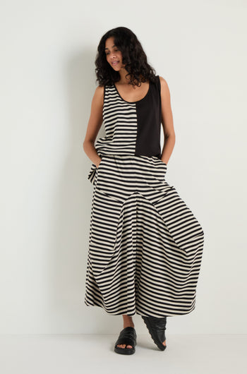 A woman stands against a white wall wearing a black and white sleeveless top paired with Stripe Balloon Trousers and black sandals.