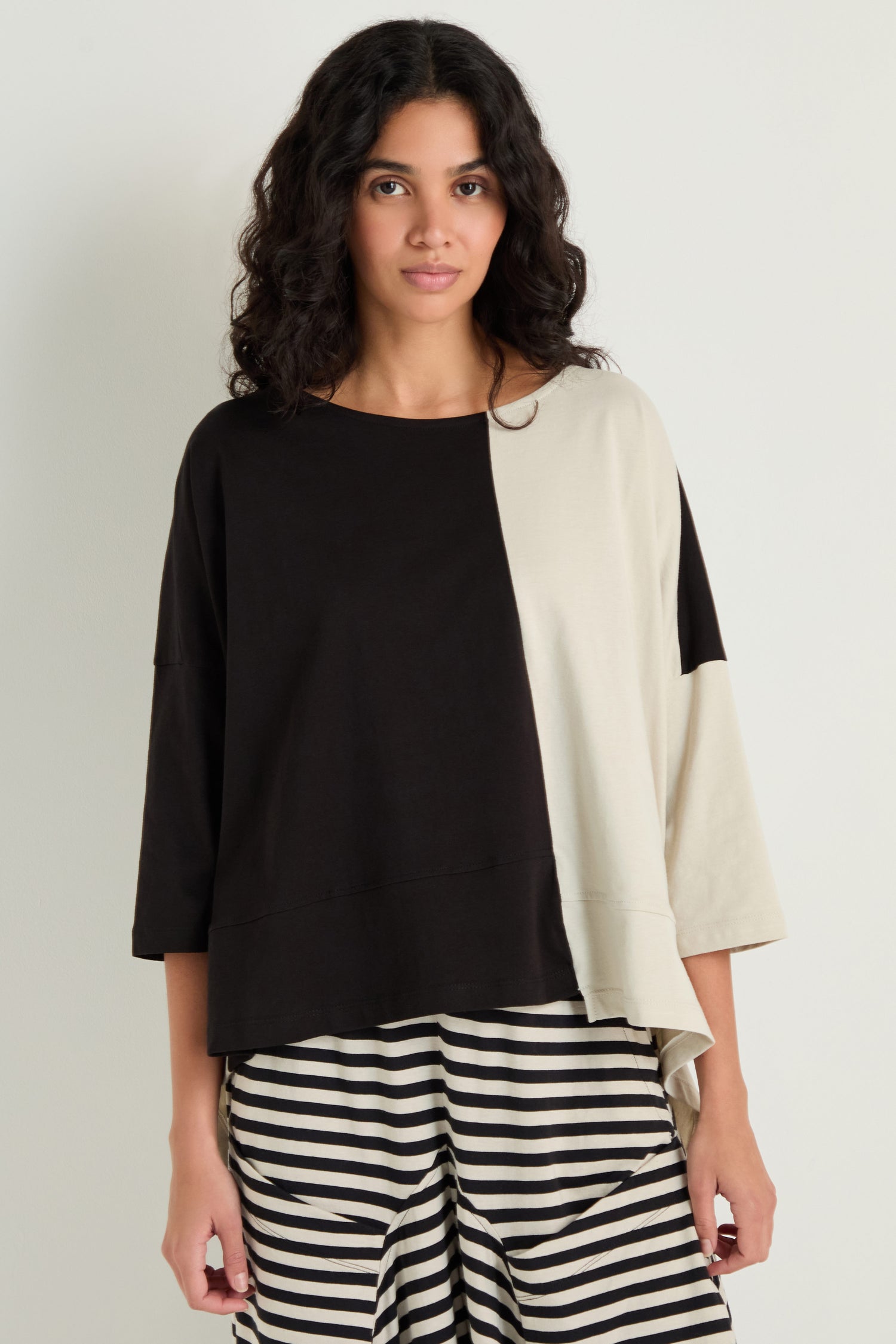 A person wears the Two-Tone Jersey Top, featuring wide sleeves and a relaxed drape, paired with black and white striped pants against a plain light background.