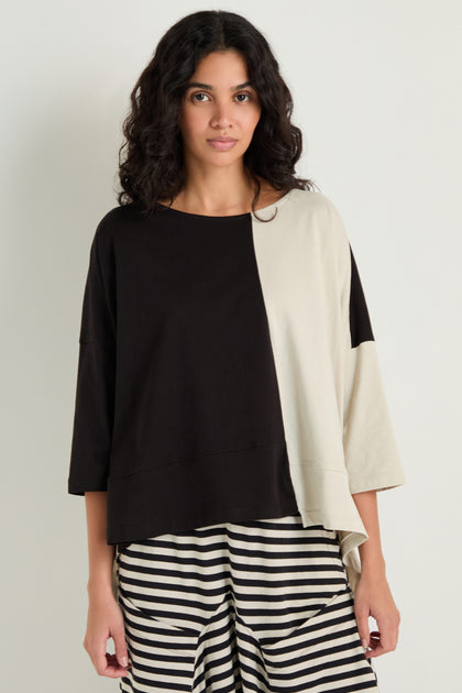 A person wears the Two-Tone Jersey Top, featuring wide sleeves and a relaxed drape, paired with black and white striped pants against a plain light background.