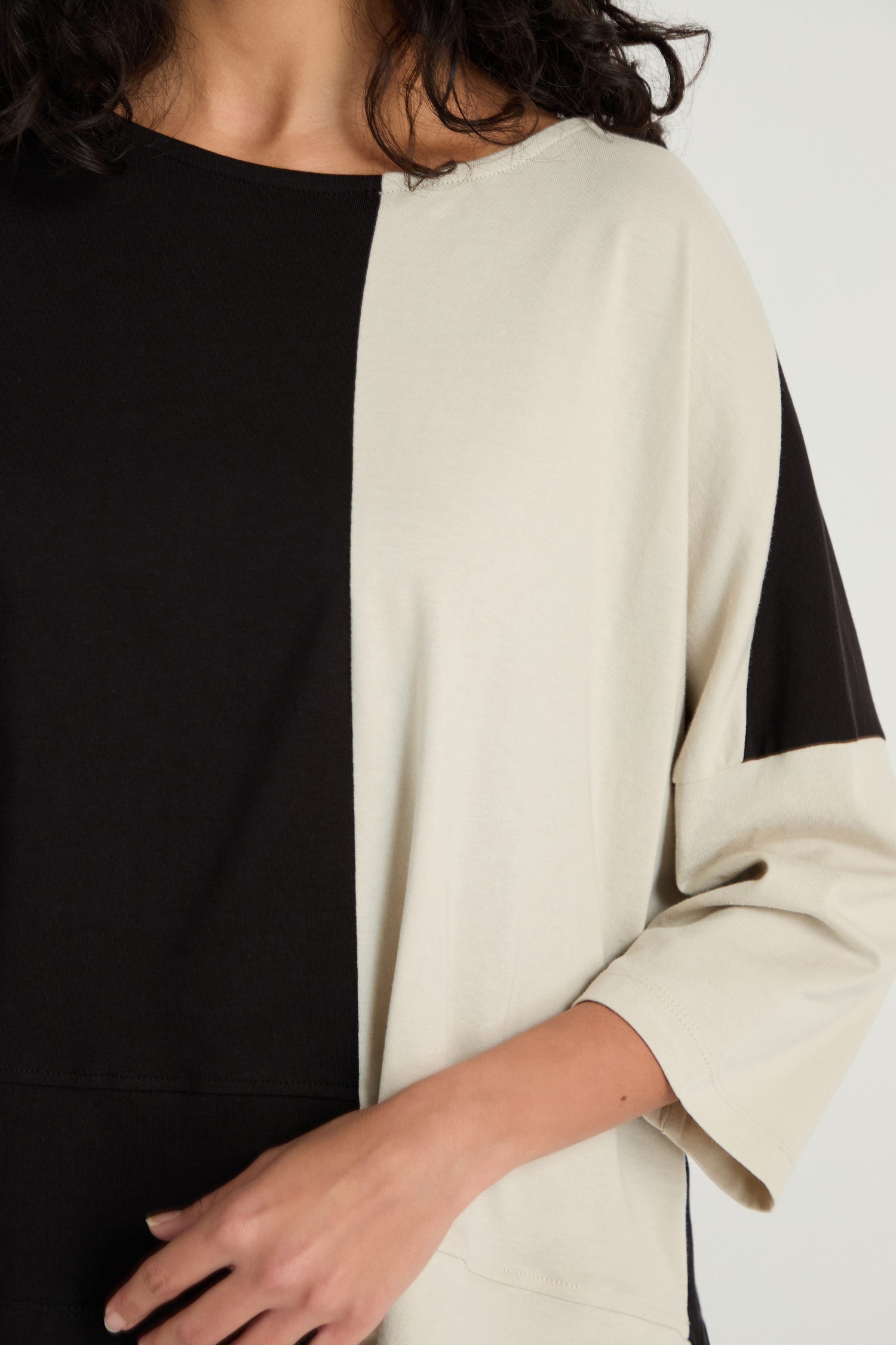 A person wears a Two-Tone Jersey Top featuring black and off-white panels, a loose fit, relaxed drape, and three-quarter length sleeves. Only the upper body is visible.