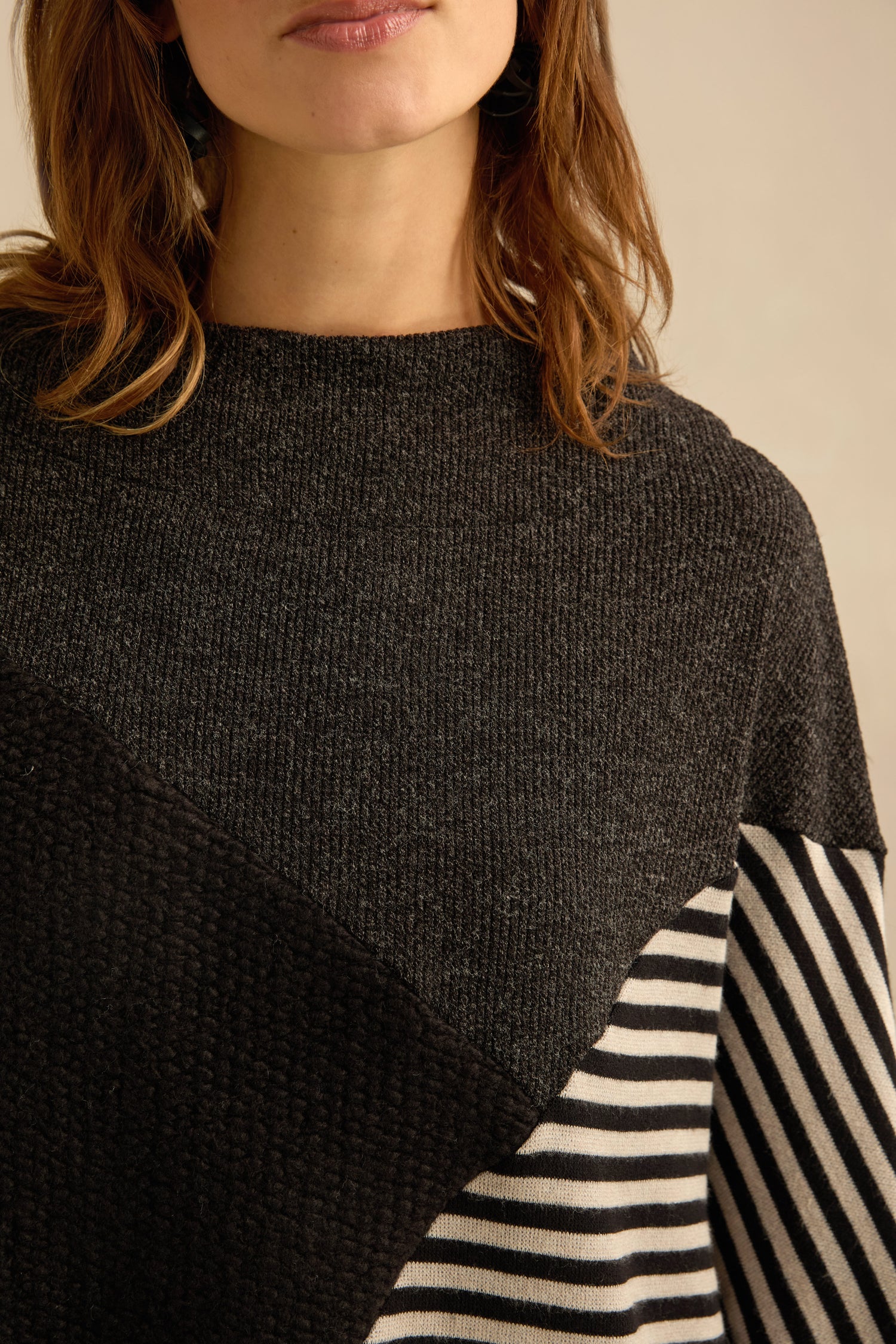 A woman wearing the Mixed Stripe Top—a dark colorblock sweater with a solid black section, a contrasting black-and-white striped panel, and an asymmetric design for a modern touch.