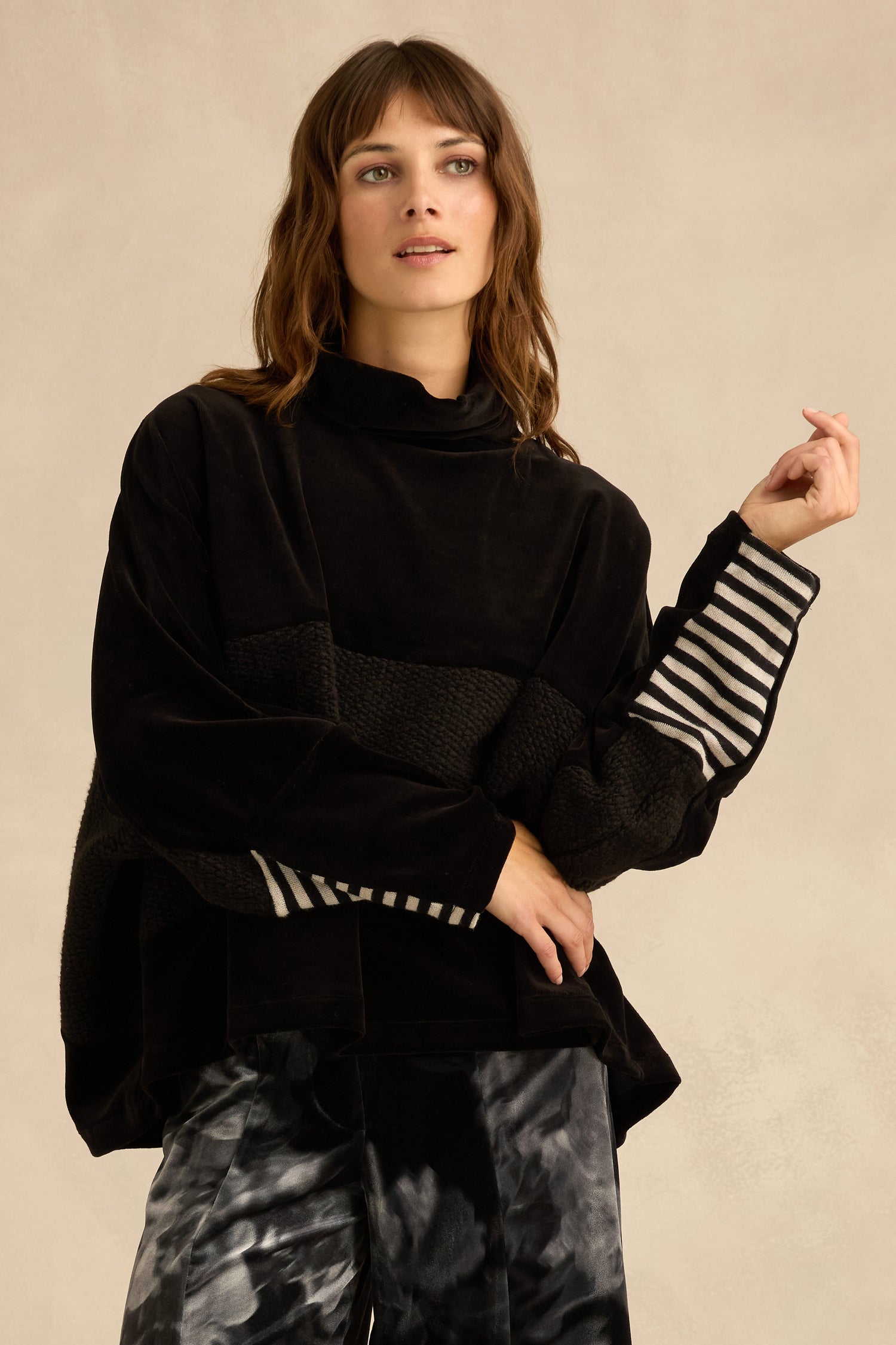 A woman models the Cowl Neck Velvet Jersey Top, featuring a loose black cowl neck and striped sleeves, paired with black-and-white tie-dye pants and set against a neutral background.