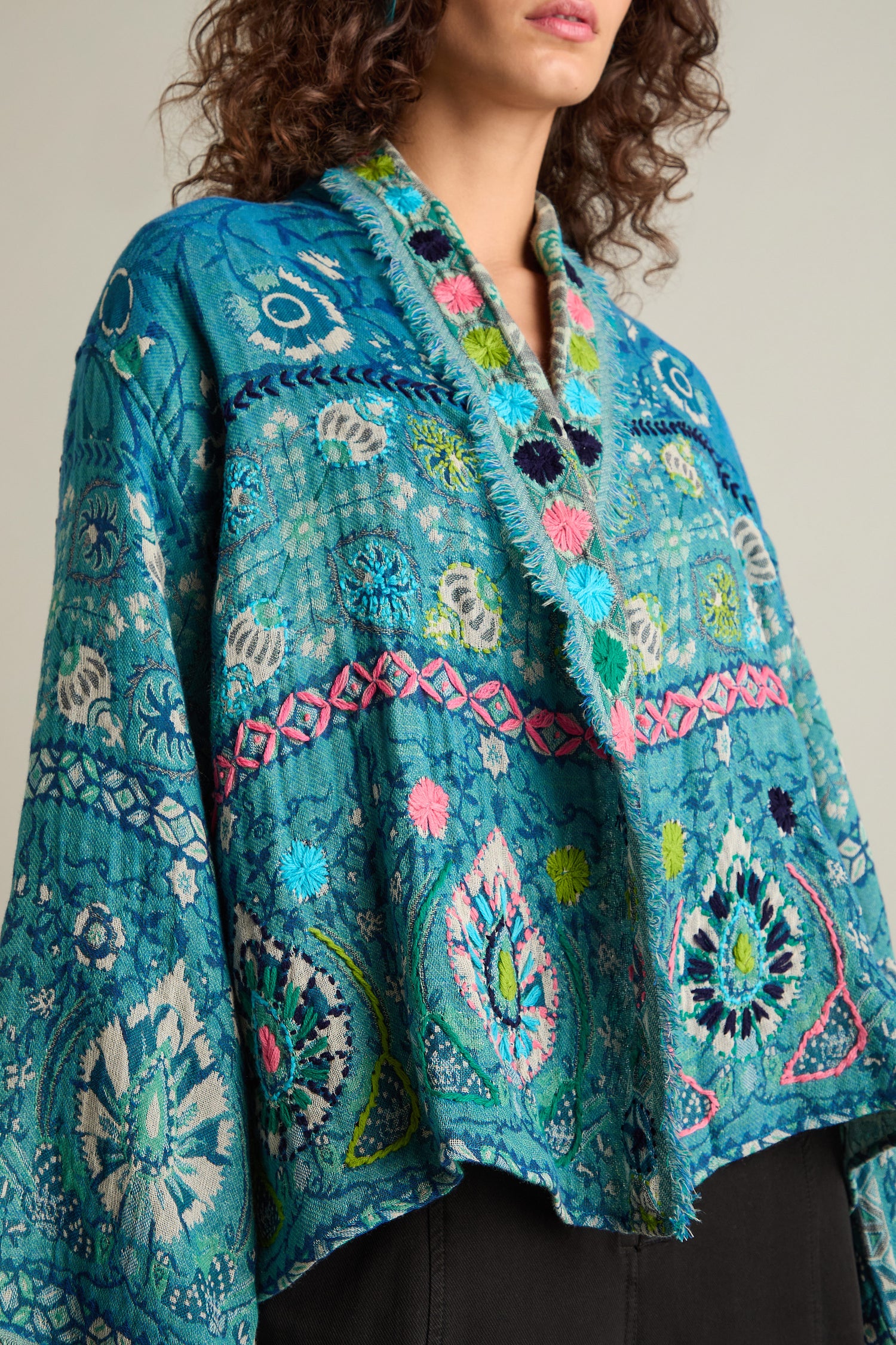 A person wearing a Cerulean Hand Embroidered Jacket with intricate floral and geometric designs, paired with dark pants.