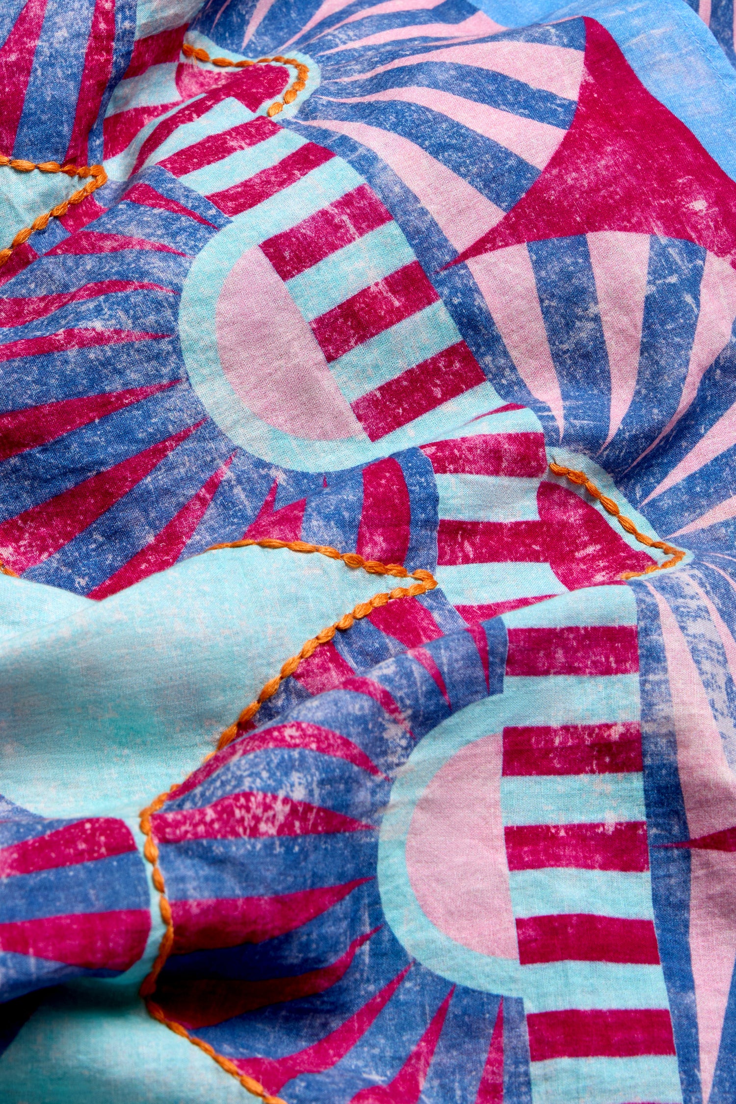 A close-up of the Embroidered Parasols Cotton Scarf, showcasing a pink, blue, and turquoise geometric pattern with orange stitched seams and delicate embroidered detailing.