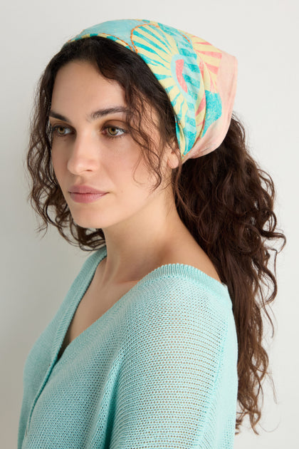 Woman with long curly hair wears the Embroidered Parasols Cotton Bandana and a light blue knit top, looking slightly to the side against a plain background.