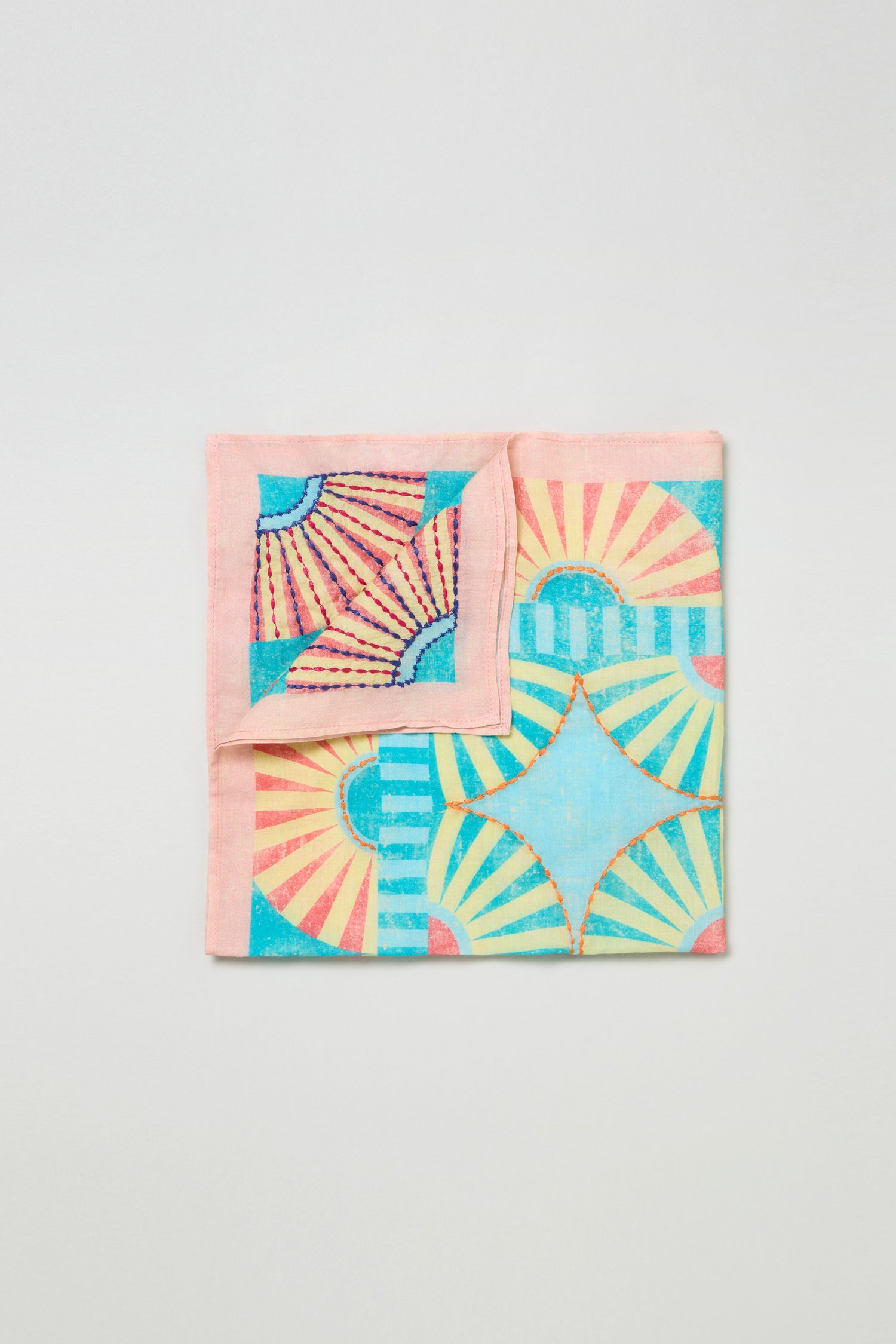 The Embroidered Parasols Cotton Bandana is a square cotton accessory with a folded corner, showcasing vibrant geometric sunburst and star designs in pink, blue, yellow, and teal.