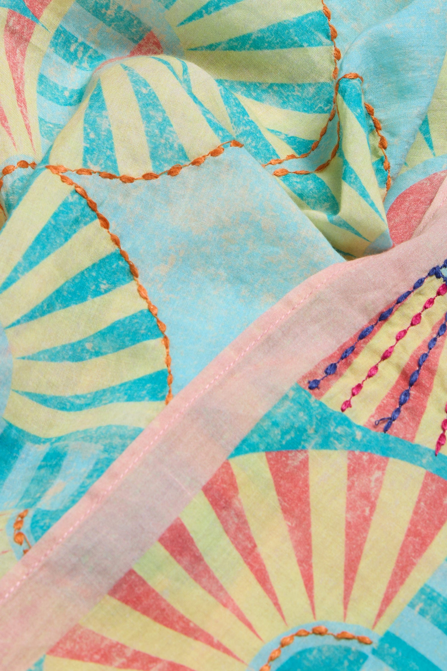 Close-up of the Embroidered Parasols Cotton Bandana, showcasing a vibrant sunburst pattern in blue, yellow, and red with orange and blue embroidered seams and a subtle parasol motif.