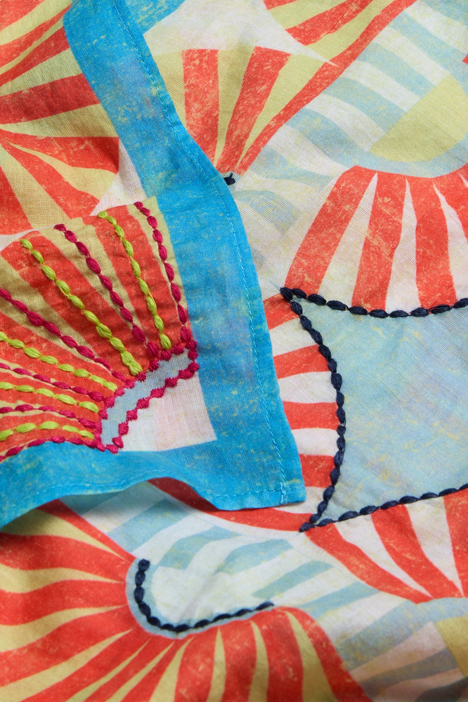 Close-up of the Embroidered Parasols Cotton Bandana, showcasing a vibrant sunburst pattern in red, yellow, blue, and green on soft cotton with visible hand-stitched embroidery in contrasting thread.