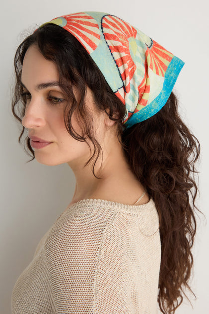 A woman with wavy brown hair wears the Embroidered Parasols Cotton Bandana and a beige knit top, posing in profile against a plain light backdrop.