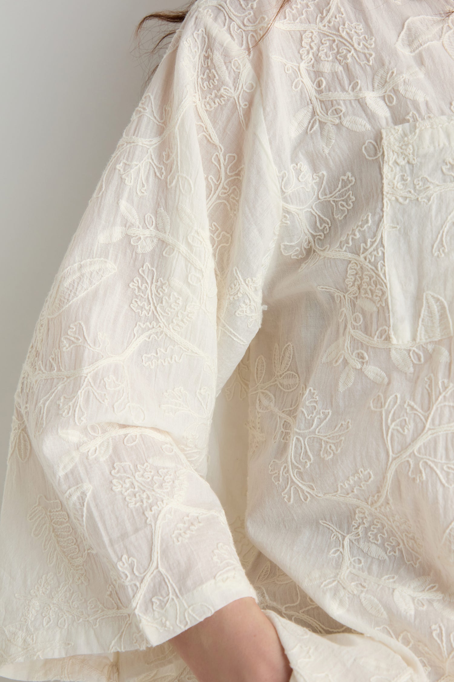 Close-up of the Embroidered Long Floral Shirt, a women's lightweight cream-colored top featuring floral embroidery, highlighting the sleeve and part of the torso.