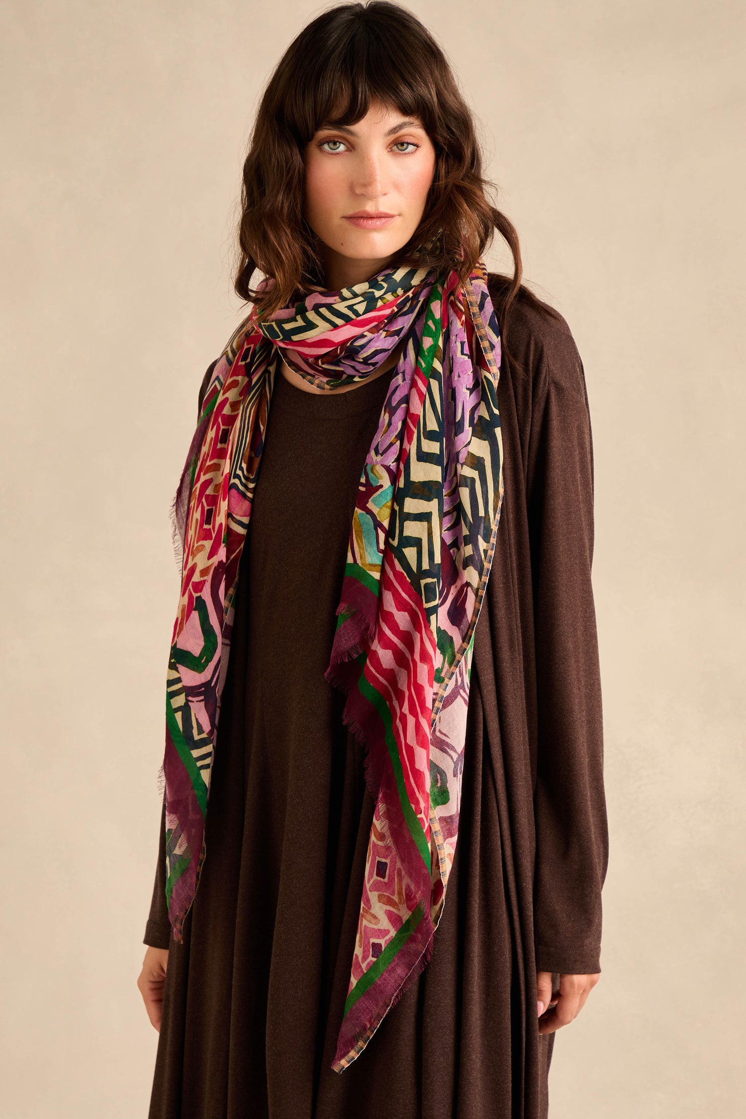 A woman wearing a long brown dress and the Graphic Print Wool Scarf stands against a neutral background, looking at the camera.