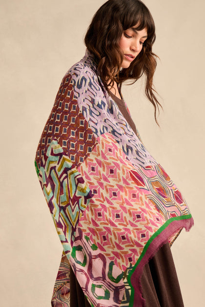 A woman with wavy brown hair wears a Graphic Print Wool Scarf over a brown outfit, standing against a neutral background.