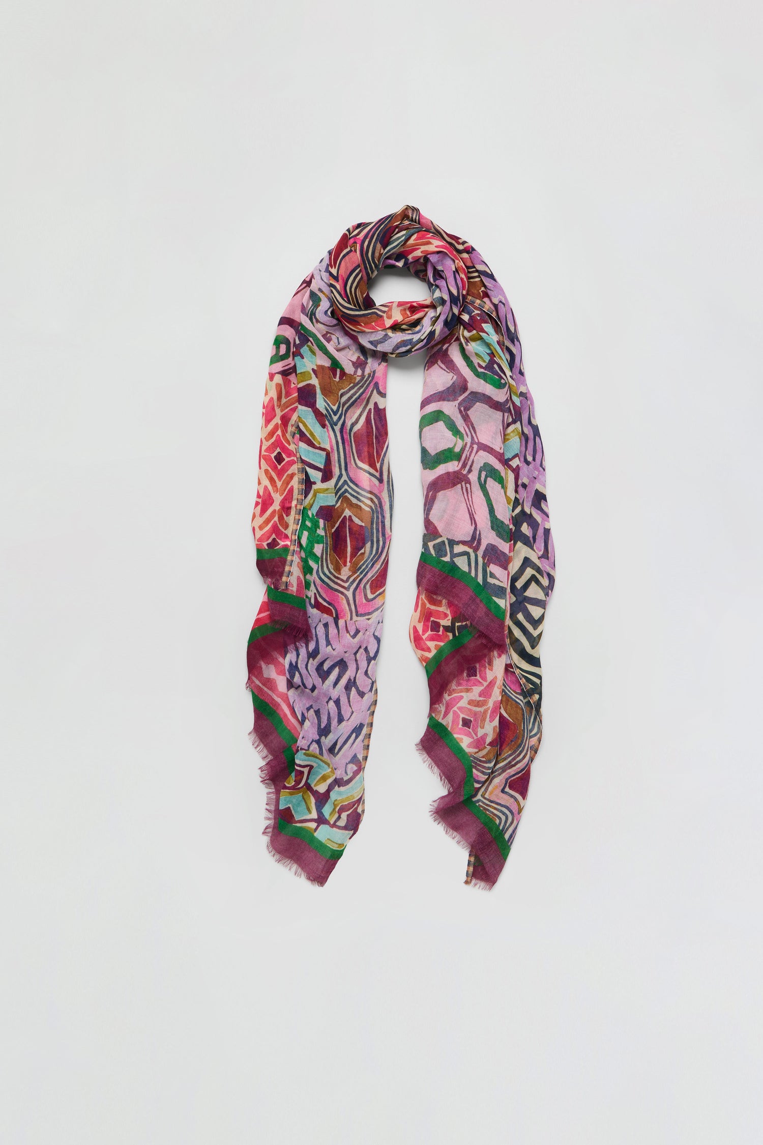 The Graphic Print Wool Scarf features vibrant geometric and abstract patterns in shades of red, pink, green, and purple, showcased against a plain white background.