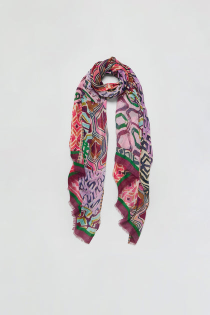 The Graphic Print Wool Scarf features vibrant geometric and abstract patterns in shades of red, pink, green, and purple, showcased against a plain white background.