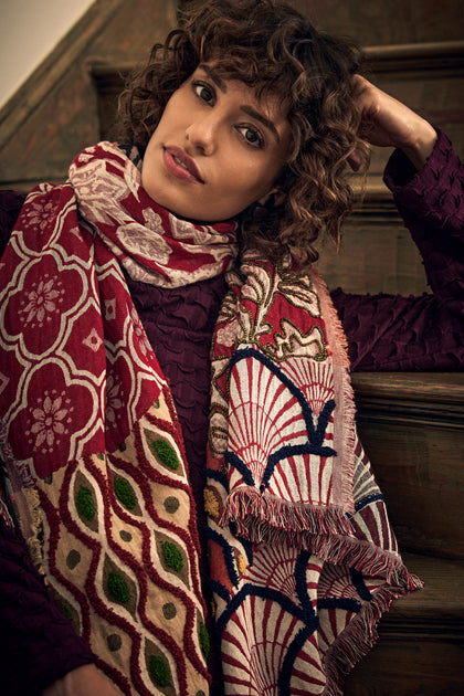 A person wears an Embroidered Cotton Wool Scarf featuring a multi-colored pattern of geometric and floral motifs with fringed edges.