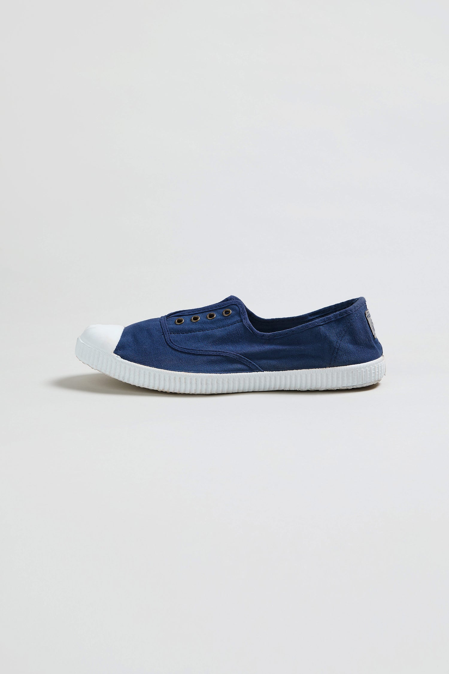 The Inglesa Navy Pumps are canvas trainers made in Spain with a white rubber toe cap and sole, eyelets for laces but no laces included, shown against a plain light background.