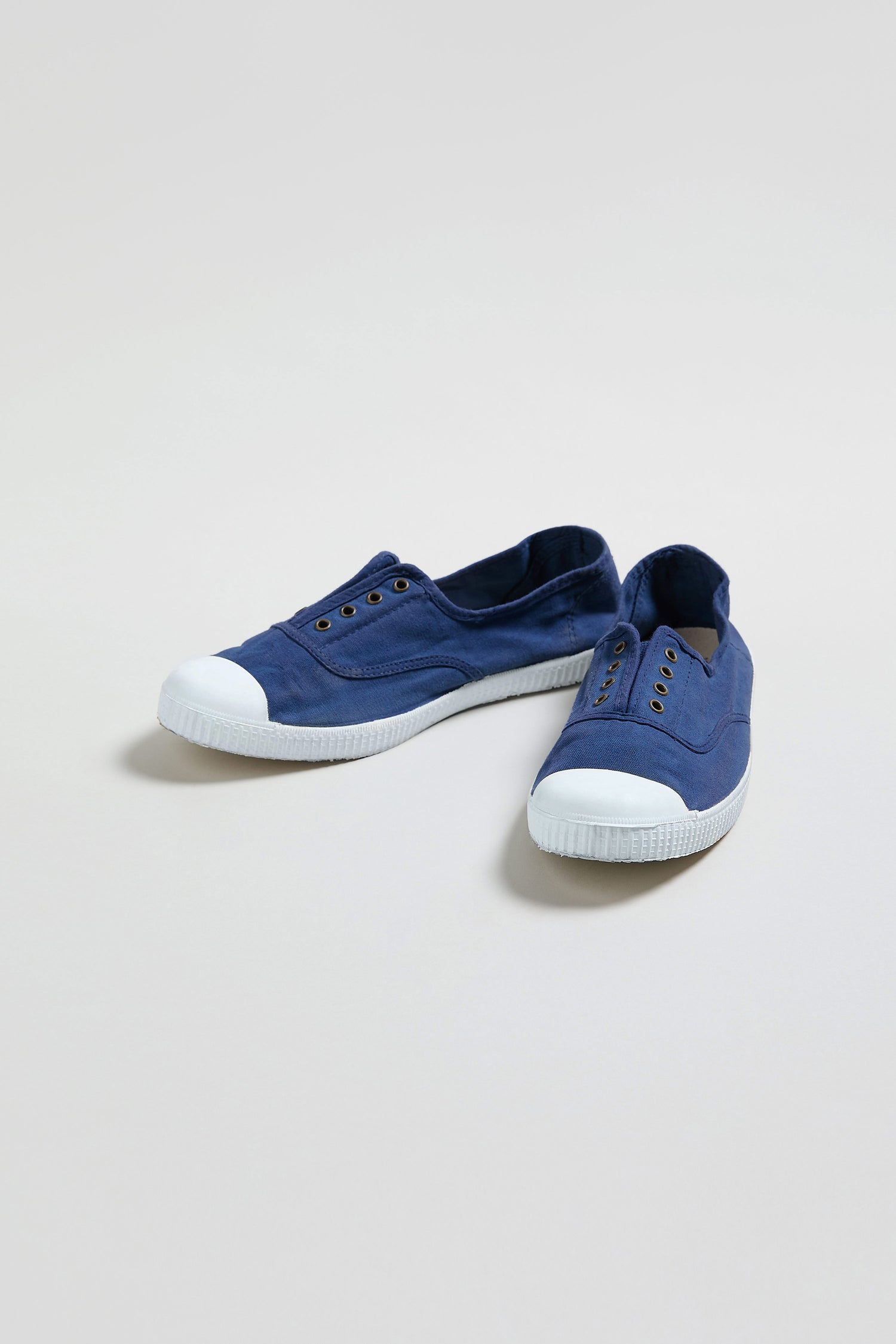 The Inglesa Navy Pumps are blue canvas trainers made in Spain from recycled cotton, with white rubber toe caps and soles, displayed on a light background.