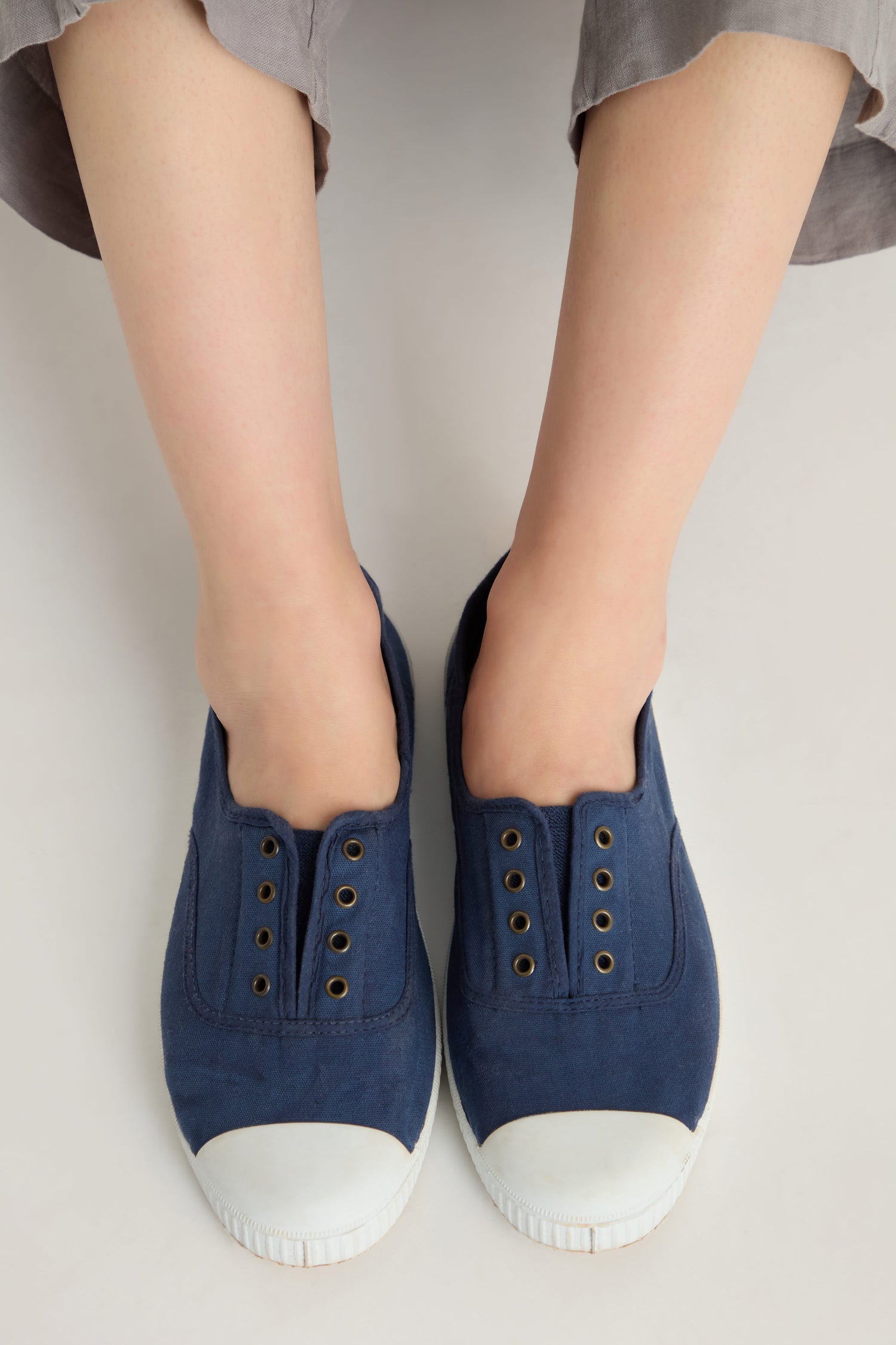A person wearing Inglesa Navy Pumps made in Spain sits with legs slightly apart on a light background.