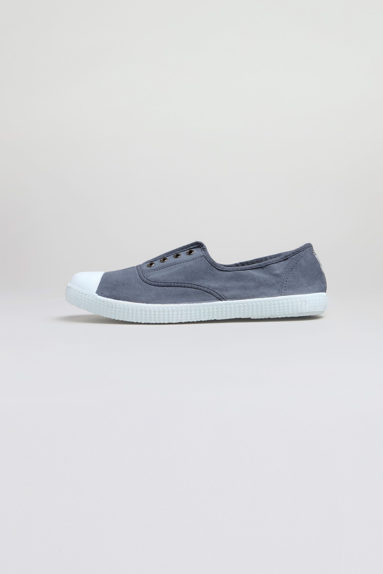 The Inglesa Slate Pumps are gray slip-on canvas trainers with a white rubber toe cap and sole, shown from the side against a plain light background.