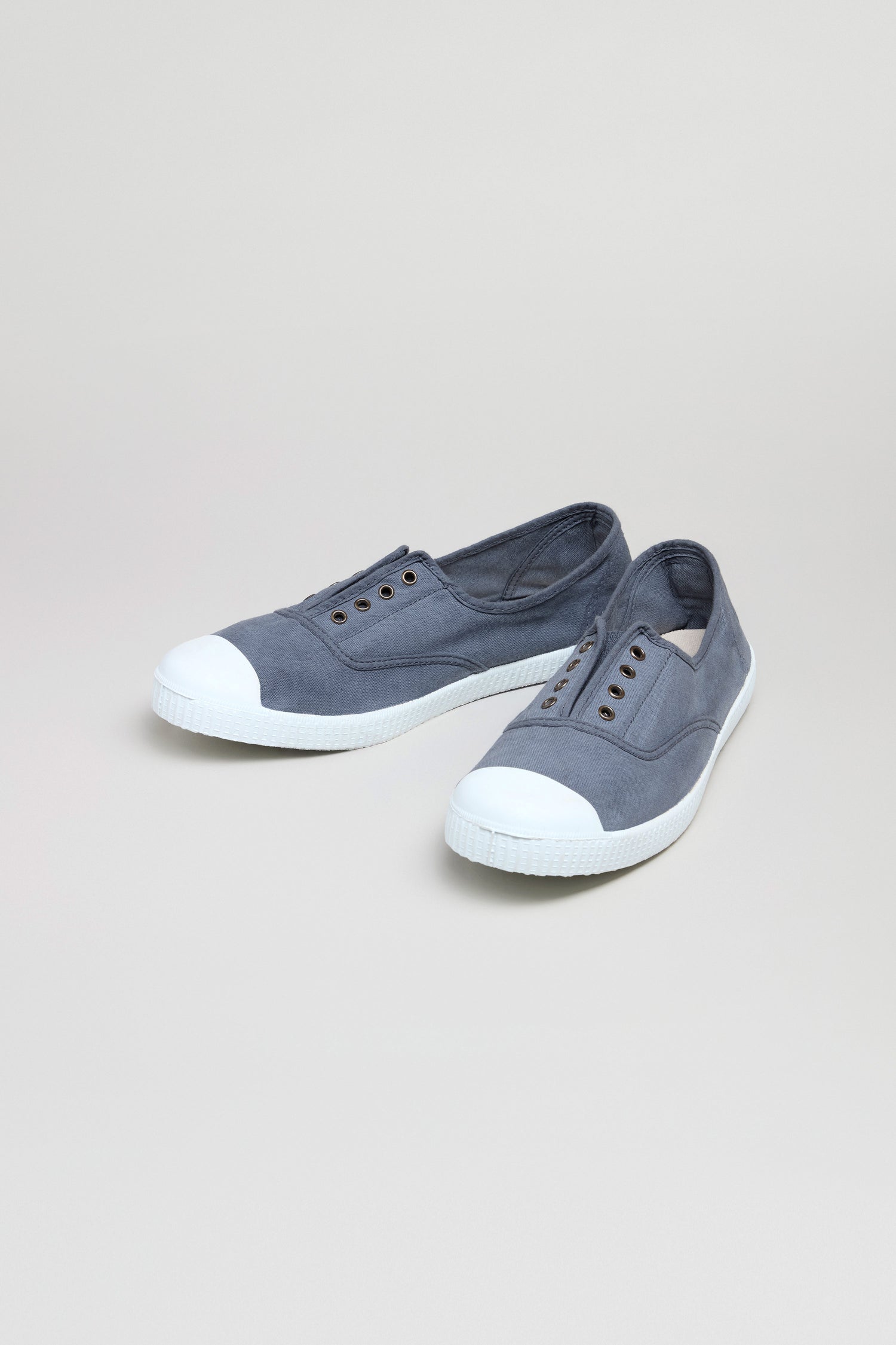 Inglesa Slate Pumps, gray slip-on canvas trainers with white rubber toe caps and soles, made in Spain, shown against a plain light background.