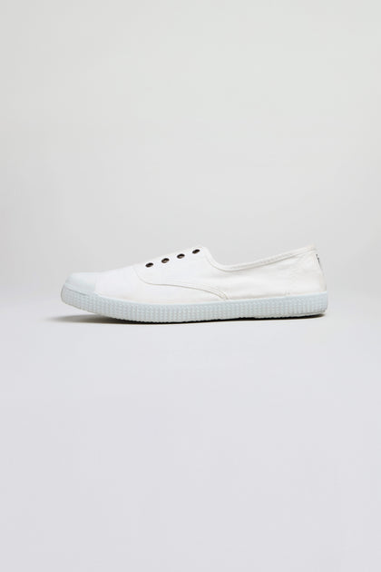 The Inglesa White Pumps, classic trainers made from recycled DREC cotton with a rubber sole and four eyelets, are shown in profile against a light gray background.