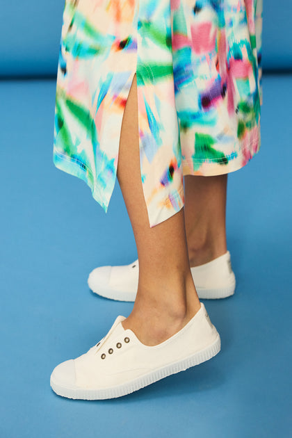 A person in a colorful, abstract-patterned skirt and Inglesa White Pumps stands on a blue floor.