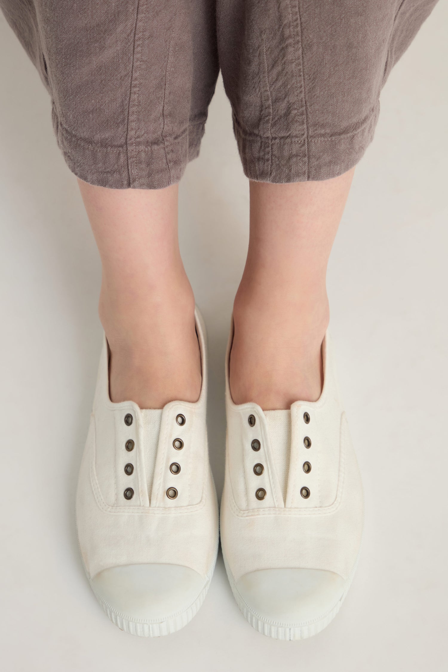 A person in loose brown pants stands barefoot inside oversized Inglesa White Pumps, crafted from recycled cotton canvas, on a light background.