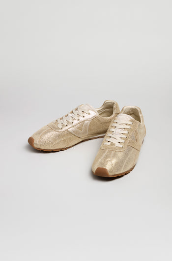 The Aster Leather Trainers are beige lace-up shoes featuring a shiny metallic cowhide leather finish and light brown rubber soles, shown against a plain white background.