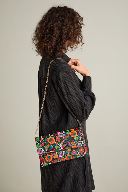 Side profile of a person with curly hair wearing a dark dress and holding the Full Bloom Hand Beaded Clutch Bag, featuring a chic chain strap and floral beauty.