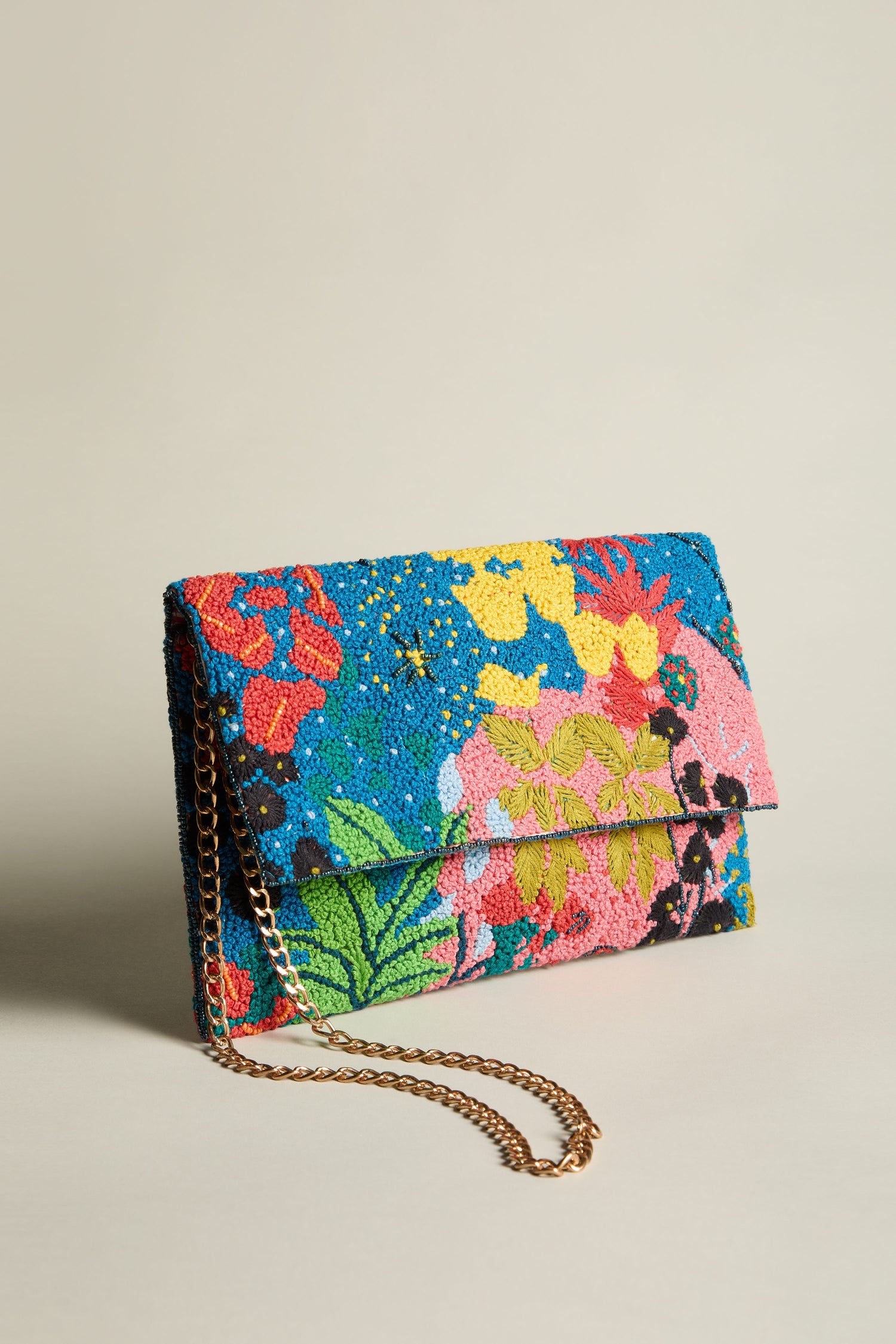 The Full Bloom Hand Beaded Clutch Bag, showcasing a vibrant floral beauty pattern and featuring a gold chain strap, is elegantly set against a neutral background.