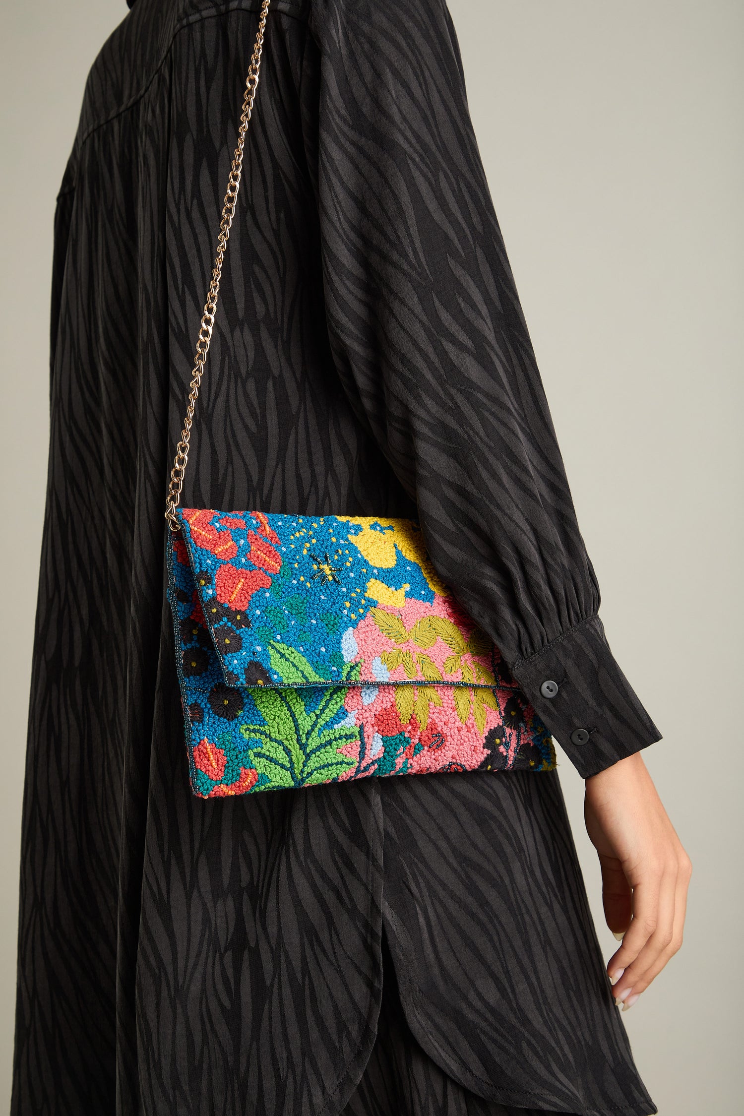 A person in a patterned black dress holds the chic Full Bloom Hand Beaded Clutch Bag, showcasing its floral beauty.