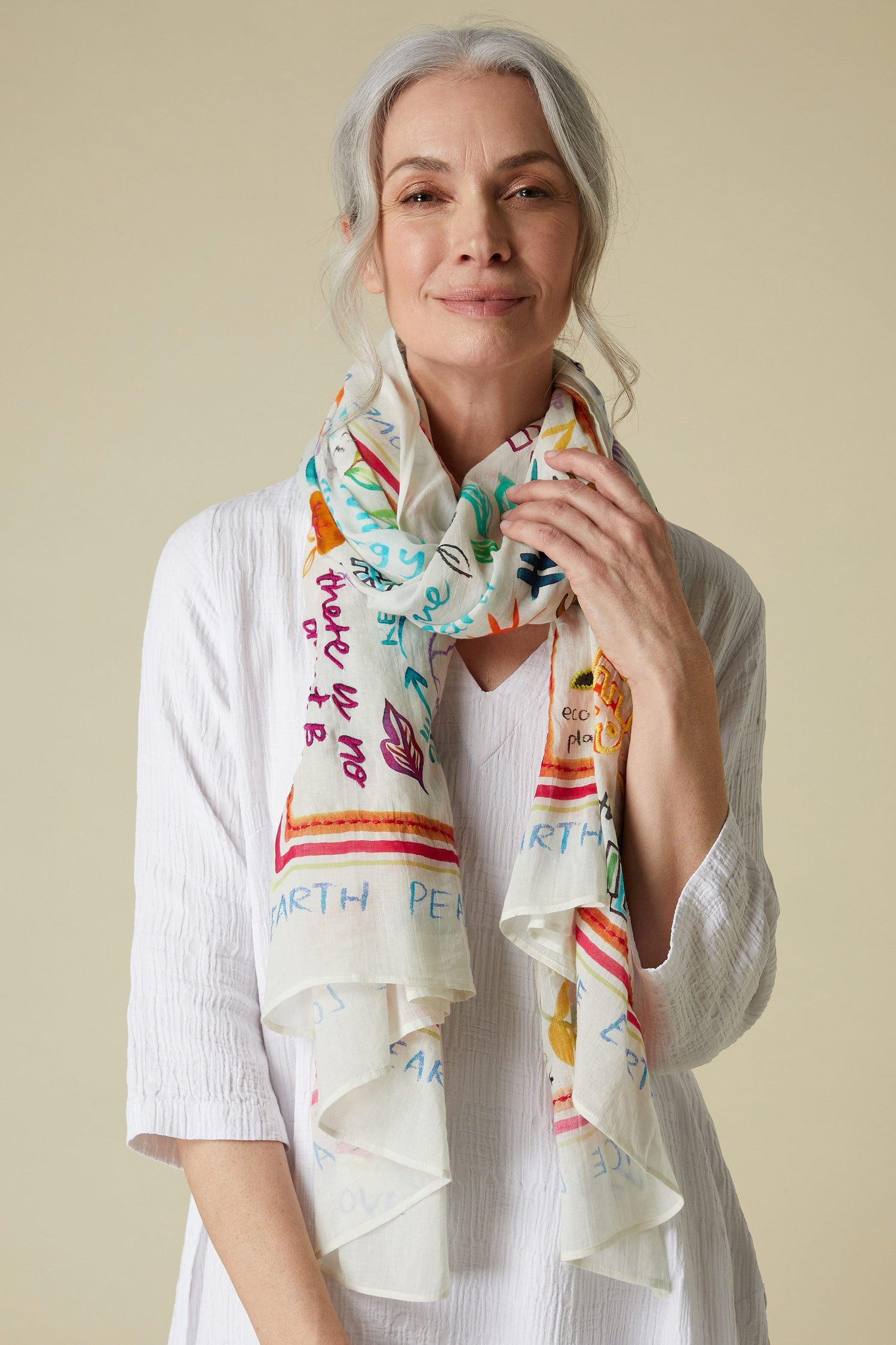 Mature woman with gray hair posing in a white blouse and Peace Earth Love Printed Cotton Scarf.