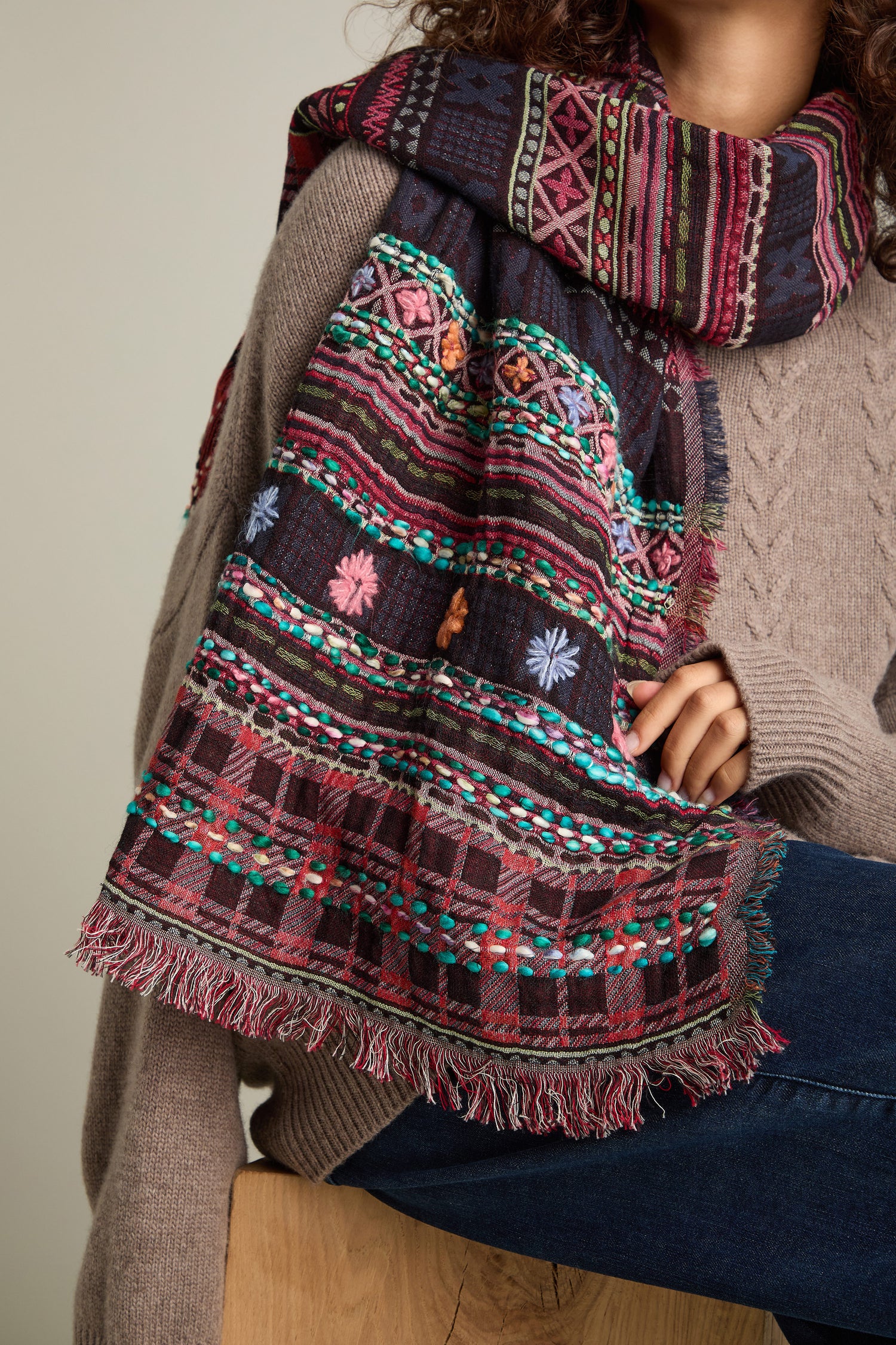 A person adorned with a Hand Embroidered Cotton Scarf, wearing a brown knit sweater and blue jeans.