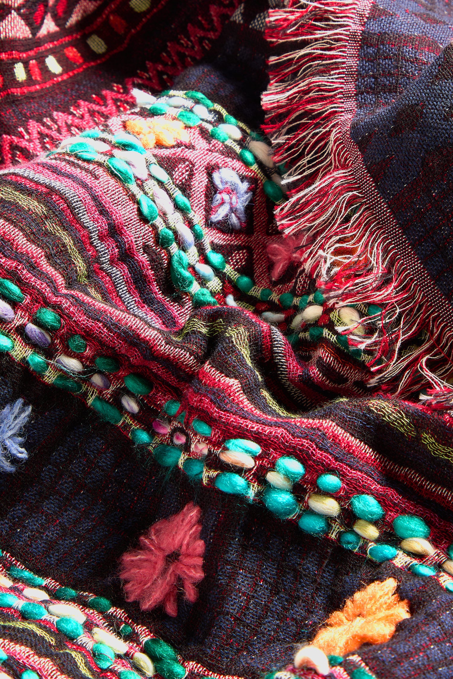 Close-up of a colorful, intricate textile featuring versatile and stylish patterns of beads, fringes, and embroidered designs in various colors, including red, green, and purple. This beautiful piece showcases the art of intricate hand embroidery on a Hand Embroidered Cotton Scarf.