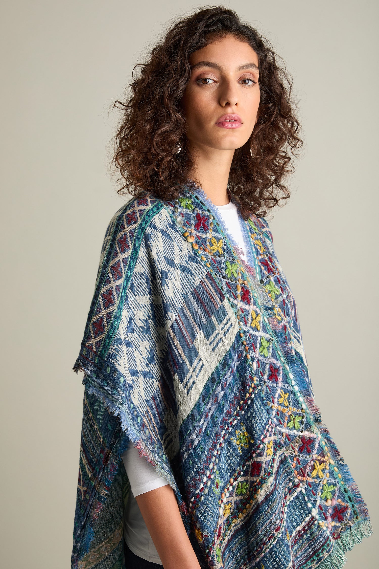 A person with curly hair is wearing an Embroidered Cotton Shawl over a white top, standing against a plain background.