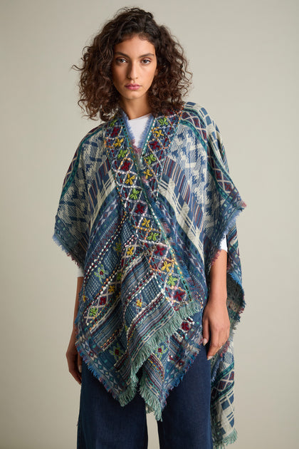 A person with curly hair wearing an intricately embroidered, multi-colored Embroidered Cotton Shawl stands against a plain background.