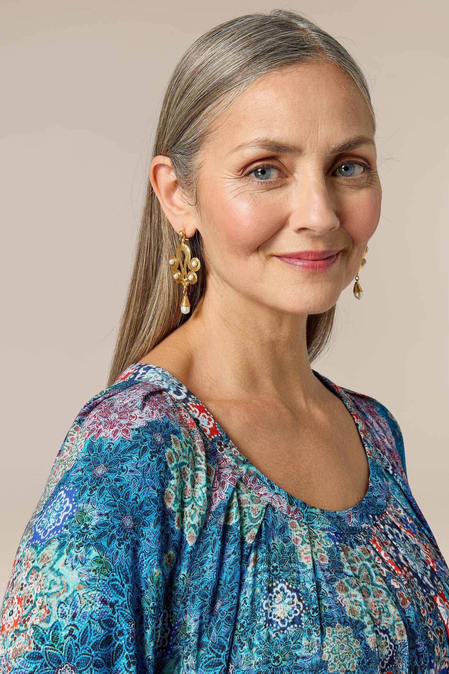 A woman in a blue and floral top, wearing Handcrafted Ottoman Earrings, posing for a photo.