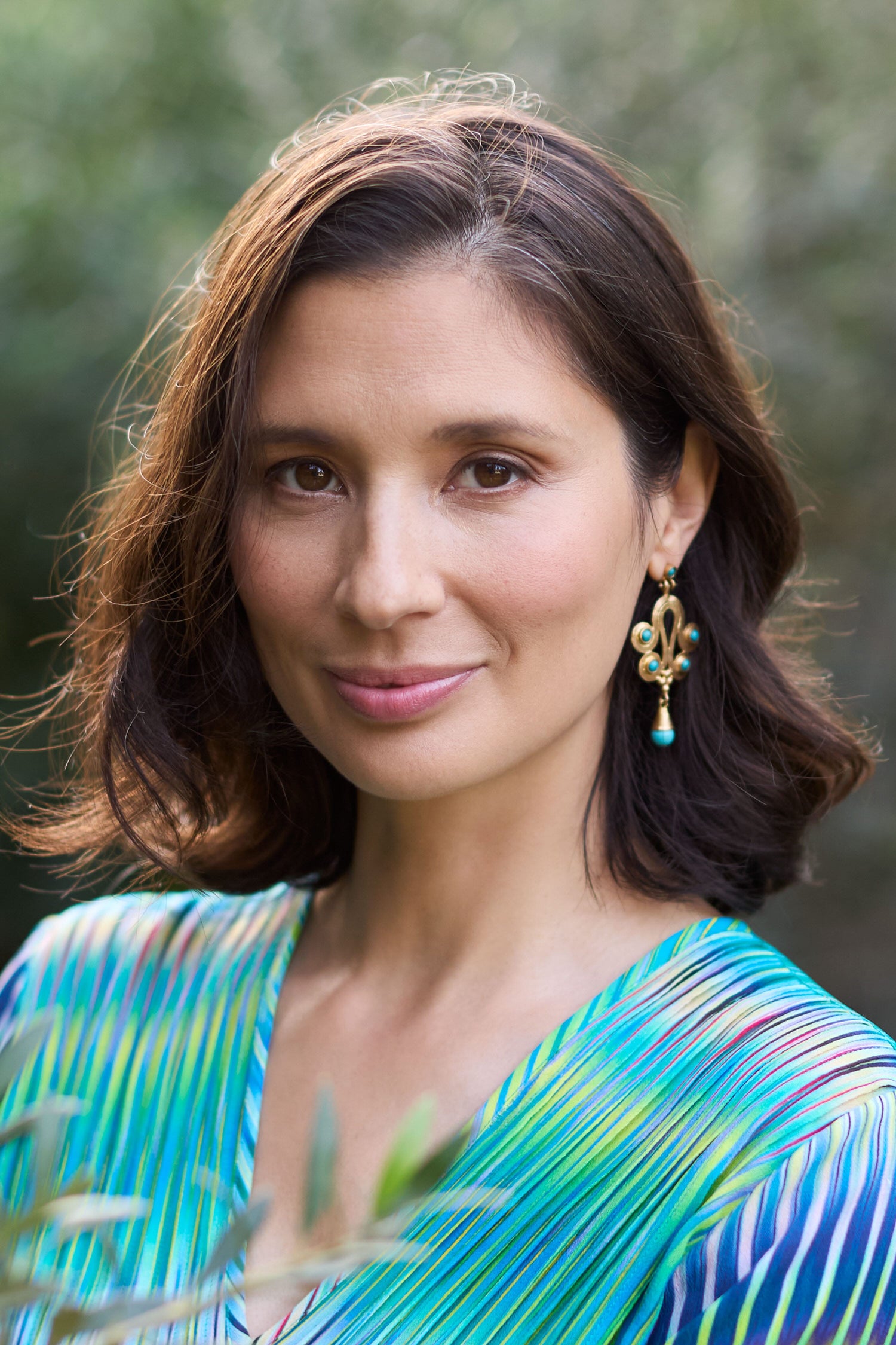 A Handcrafted Ottoman Earrings wearing a blue and green dress and earrings, showcasing wearable art.